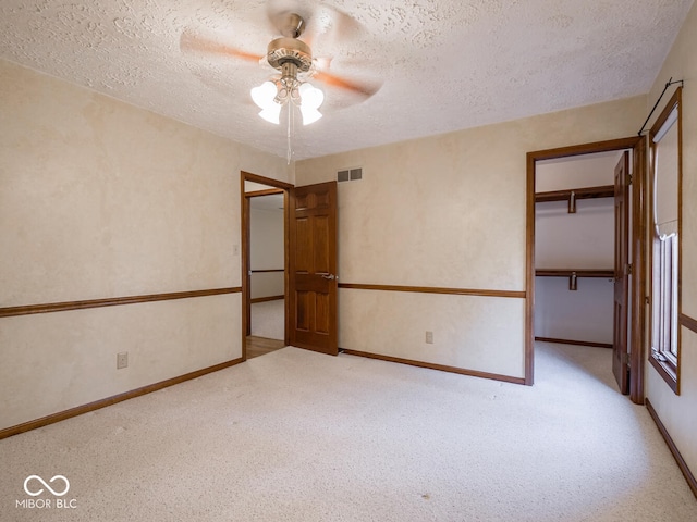 unfurnished bedroom featuring visible vents, a closet, a textured ceiling, a walk in closet, and carpet flooring