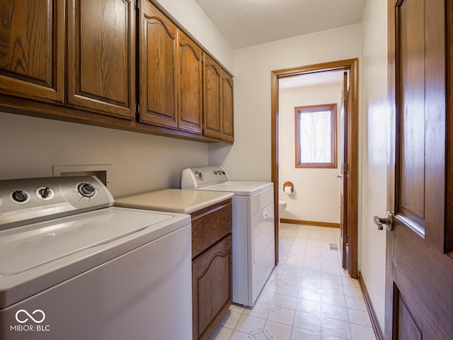 washroom featuring washer and dryer, a textured ceiling, cabinet space, baseboards, and light floors