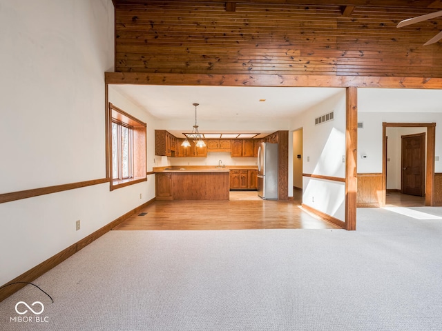 kitchen featuring brown cabinetry, visible vents, a peninsula, freestanding refrigerator, and light colored carpet