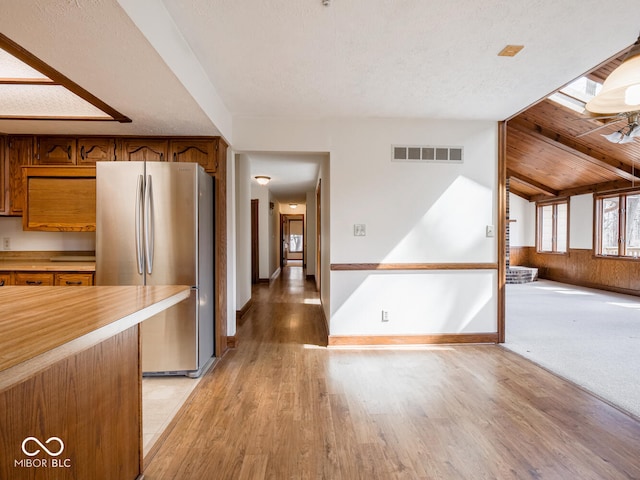 kitchen featuring visible vents, light wood-style flooring, freestanding refrigerator, brown cabinetry, and vaulted ceiling