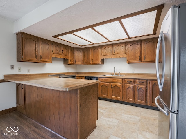 kitchen with light countertops, brown cabinets, a peninsula, stainless steel appliances, and a sink