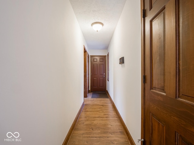 corridor featuring light wood-style floors, baseboards, and a textured ceiling