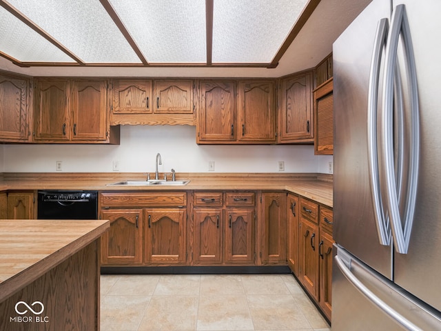 kitchen featuring butcher block countertops, dishwasher, light tile patterned floors, freestanding refrigerator, and a sink