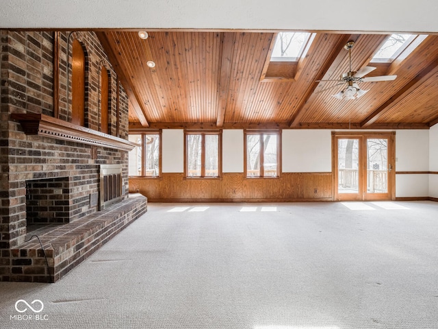 unfurnished living room with a brick fireplace, wood ceiling, a wainscoted wall, and a wealth of natural light