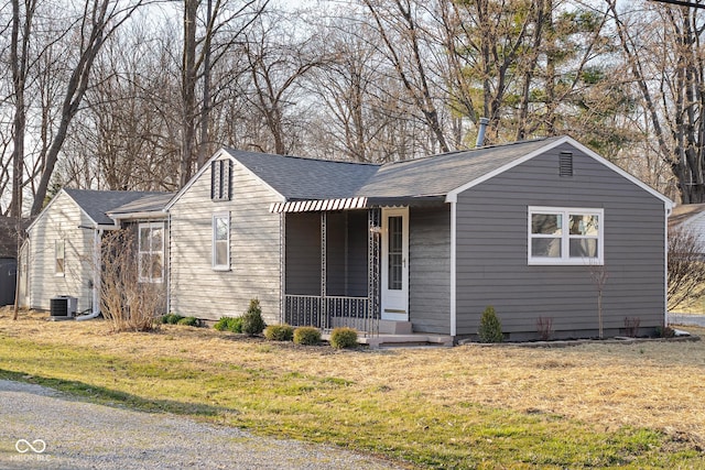 ranch-style house featuring central air condition unit, roof with shingles, a porch, and a front lawn