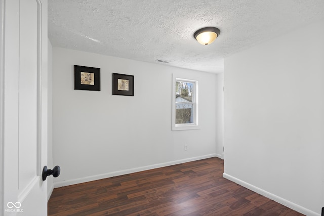 unfurnished room with visible vents, baseboards, dark wood-type flooring, and a textured ceiling