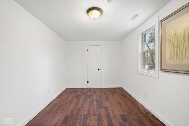 empty room featuring visible vents, baseboards, and dark wood-type flooring