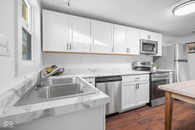 kitchen featuring dark wood finished floors, a sink, stainless steel appliances, white cabinets, and a textured ceiling