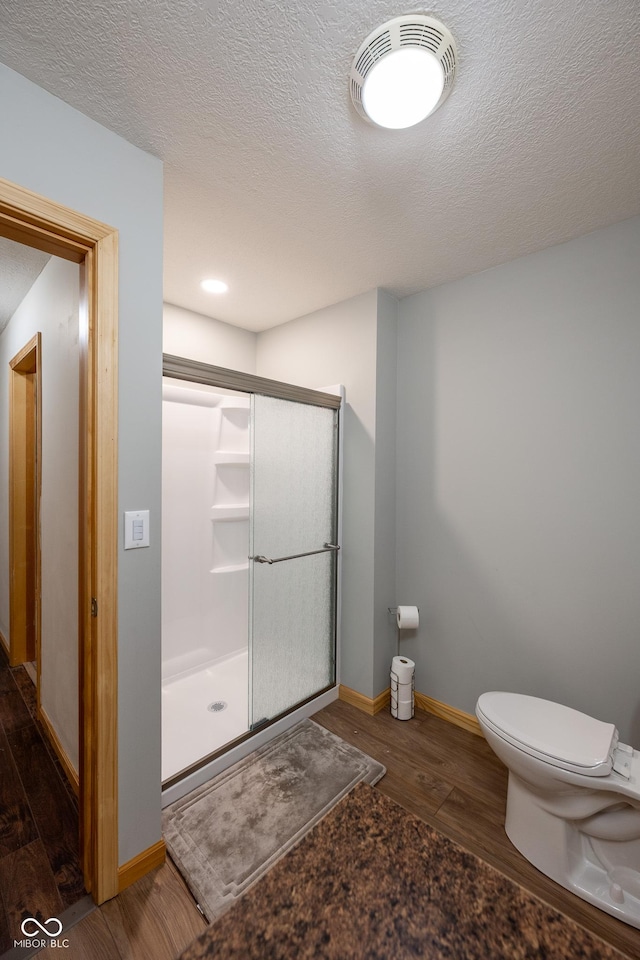 bathroom featuring a shower stall, baseboards, toilet, wood finished floors, and a textured ceiling