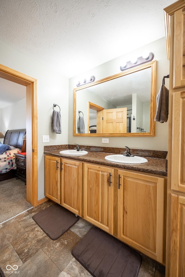 ensuite bathroom featuring double vanity, a textured ceiling, stone finish flooring, and a sink