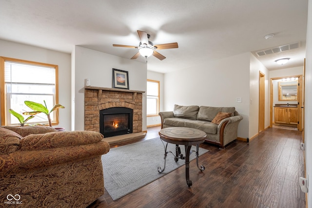 living room with visible vents, baseboards, a fireplace, a ceiling fan, and dark wood-style flooring