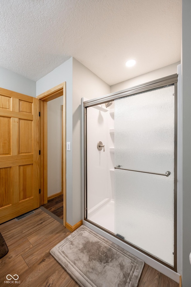 full bathroom with wood finished floors, baseboards, visible vents, a shower stall, and a textured ceiling