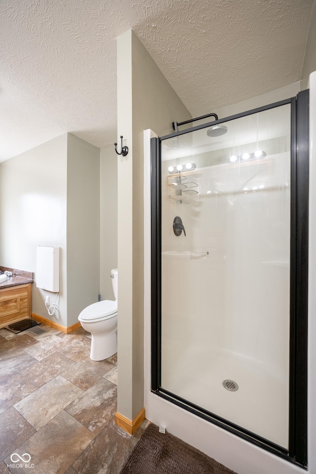 bathroom with toilet, a stall shower, a textured ceiling, stone tile flooring, and baseboards