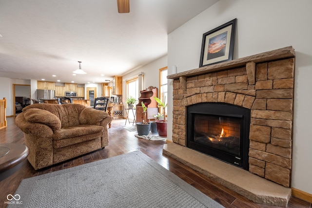 living area featuring dark wood finished floors, a stone fireplace, a ceiling fan, and baseboards