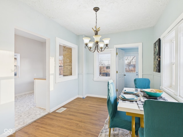 dining room with an inviting chandelier, wood finished floors, visible vents, and a textured ceiling