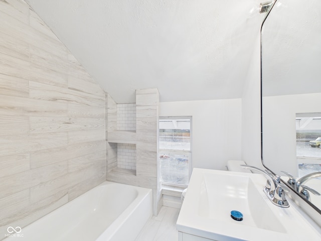 full bathroom featuring vanity, lofted ceiling, a tub to relax in, and a textured ceiling