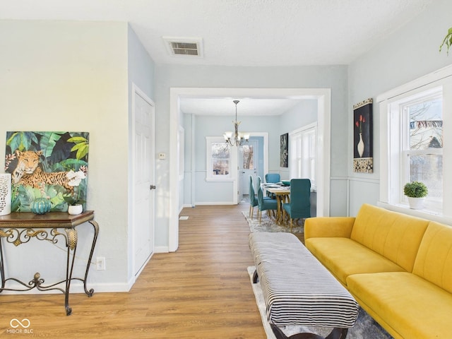 living room with a notable chandelier, visible vents, plenty of natural light, and light wood-type flooring