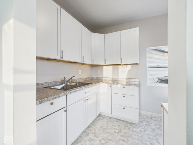 kitchen with a sink, white cabinetry, light countertops, baseboards, and light floors