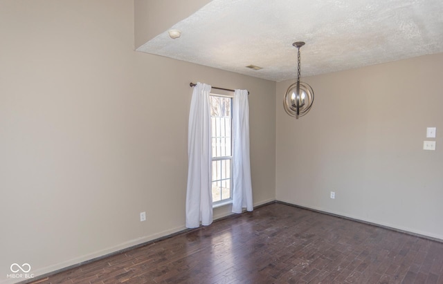 empty room with a notable chandelier, baseboards, dark wood-type flooring, and a textured ceiling