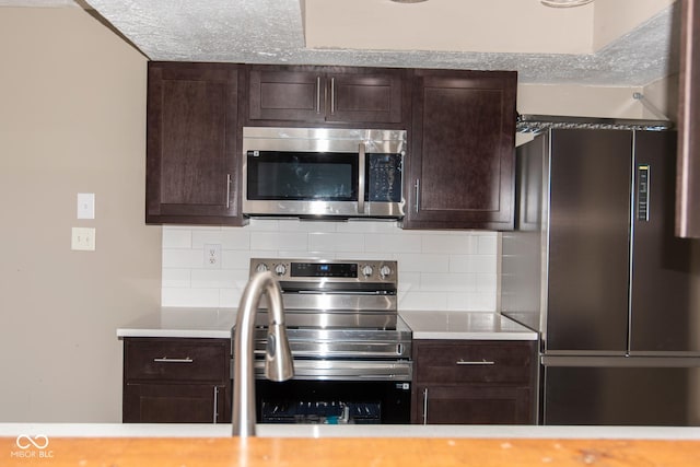 kitchen featuring dark brown cabinetry, decorative backsplash, stainless steel appliances, and light countertops