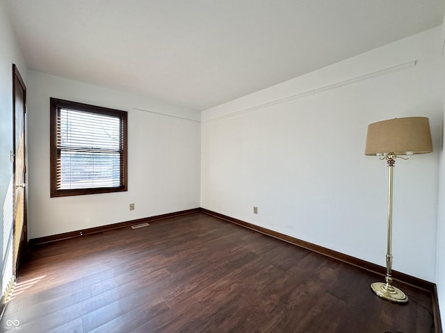 spare room with baseboards and dark wood-style flooring