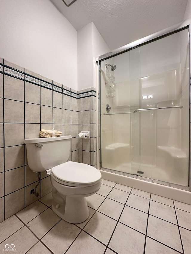 full bath featuring tile patterned floors, toilet, a stall shower, a textured ceiling, and tile walls