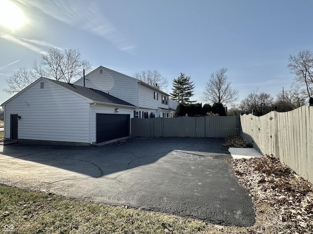 view of side of property featuring a gate, aphalt driveway, fence, roof with shingles, and a garage