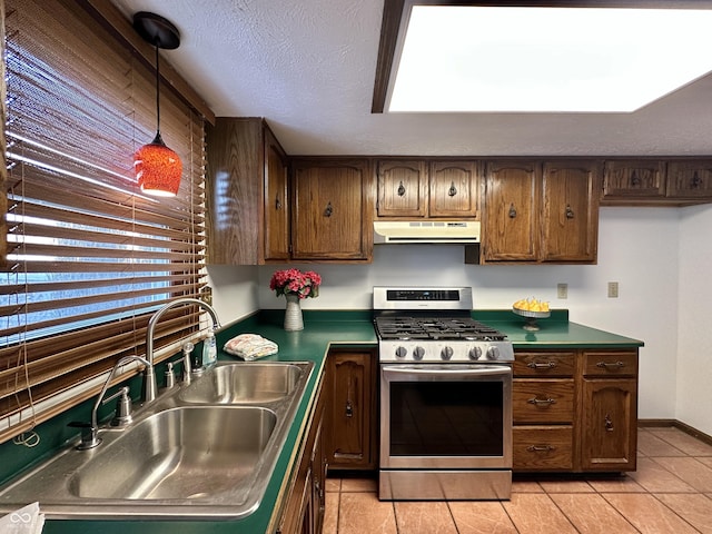 kitchen featuring stainless steel gas stove, under cabinet range hood, decorative light fixtures, a sink, and a textured ceiling