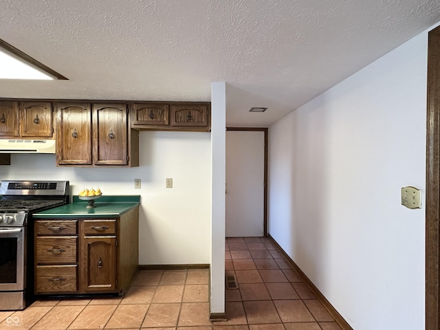 kitchen featuring under cabinet range hood, light tile patterned floors, a textured ceiling, and stainless steel gas range