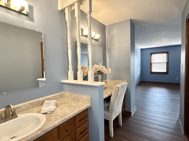 bathroom with vanity, wood finished floors, baseboards, and a textured ceiling