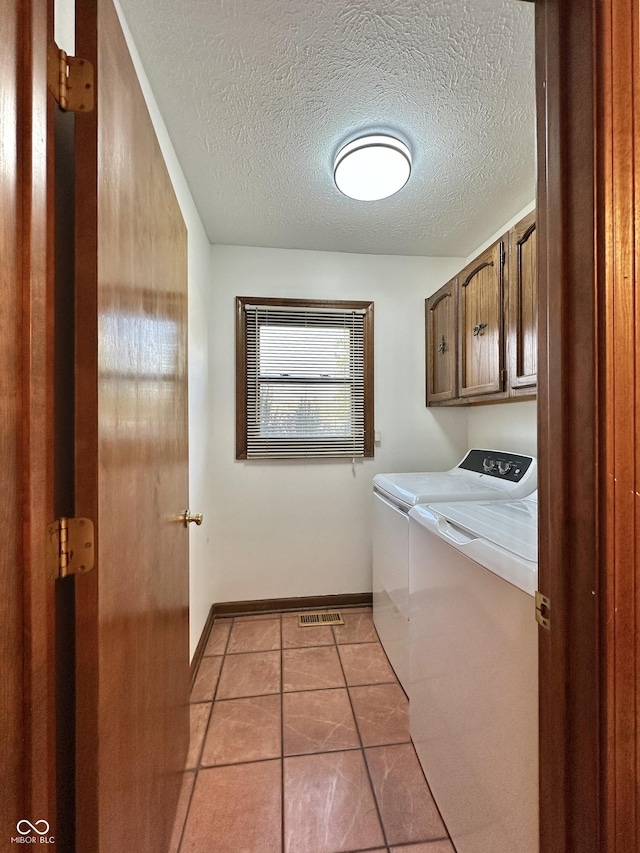 laundry area featuring baseboards, washing machine and dryer, light tile patterned flooring, cabinet space, and a textured ceiling