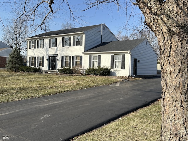 colonial inspired home featuring a front lawn, brick siding, and aphalt driveway