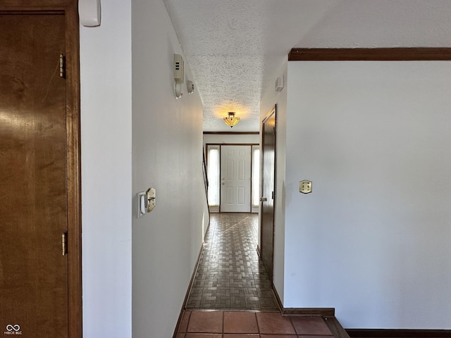 hall featuring baseboards, a textured ceiling, and tile patterned flooring