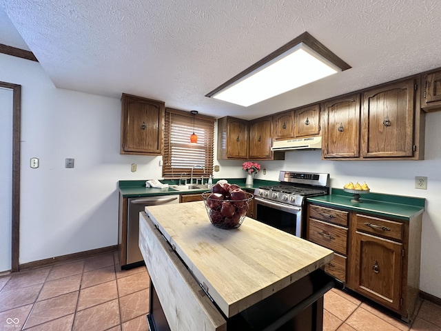 kitchen featuring under cabinet range hood, a sink, a textured ceiling, appliances with stainless steel finishes, and baseboards