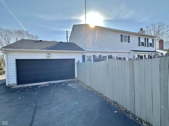 view of front of property with aphalt driveway, a garage, a chimney, and fence