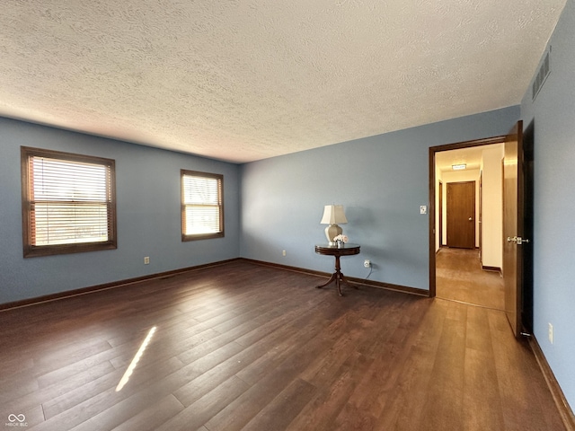 empty room featuring visible vents, baseboards, a textured ceiling, and wood finished floors