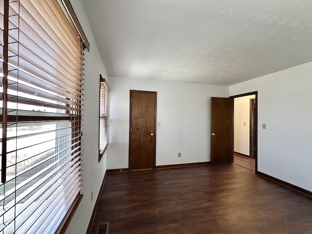 spare room featuring a textured ceiling, wood finished floors, visible vents, and baseboards