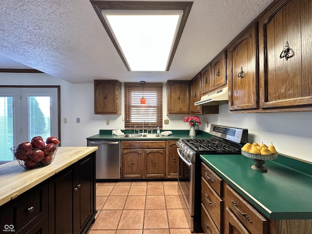 kitchen with light tile patterned floors, a sink, under cabinet range hood, a textured ceiling, and appliances with stainless steel finishes