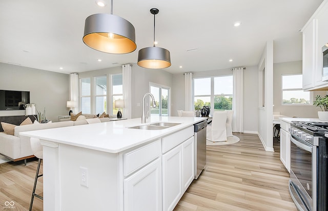 kitchen featuring light wood finished floors, open floor plan, white cabinets, stainless steel appliances, and a sink