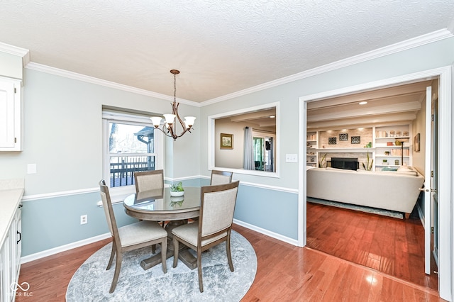 dining room featuring wood finished floors, baseboards, ornamental molding, a textured ceiling, and a chandelier