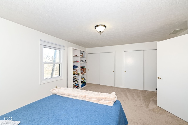 bedroom with visible vents, multiple closets, carpet floors, and a textured ceiling