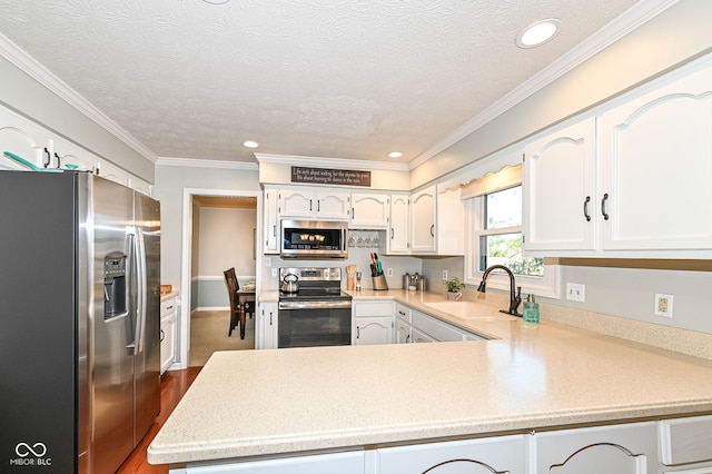 kitchen with light countertops, appliances with stainless steel finishes, a peninsula, white cabinetry, and a sink