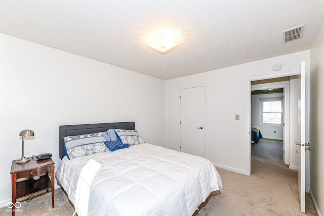 bedroom with visible vents, light colored carpet, a textured ceiling, and baseboards