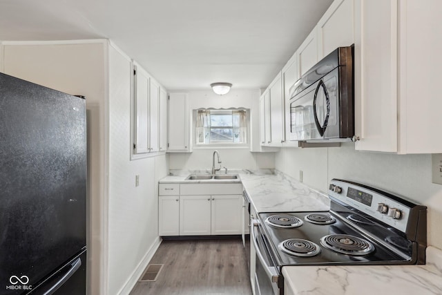 kitchen featuring white cabinetry, black appliances, light wood-type flooring, and a sink