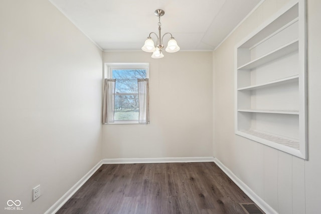 unfurnished dining area with built in features, baseboards, visible vents, dark wood finished floors, and an inviting chandelier