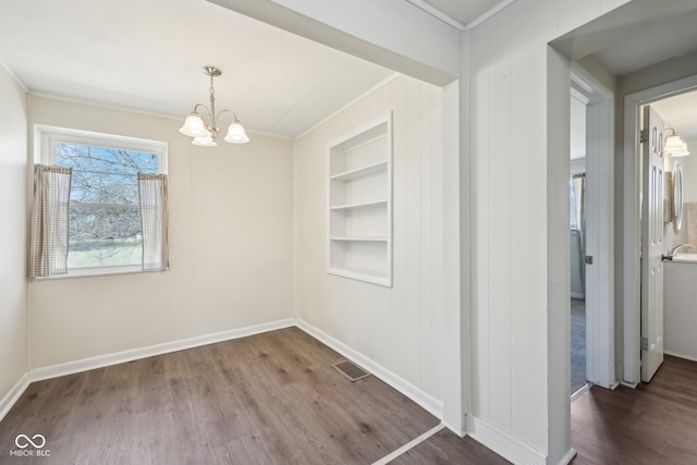 unfurnished dining area with built in features, wood finished floors, baseboards, ornamental molding, and a notable chandelier