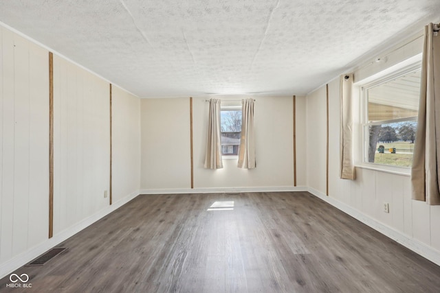 spare room featuring visible vents, baseboards, a textured ceiling, and wood finished floors