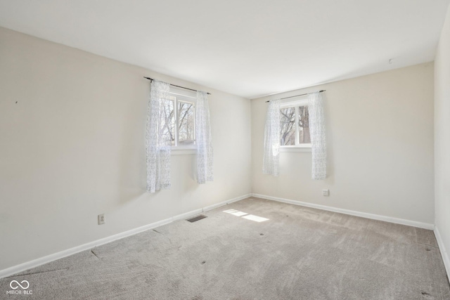 carpeted spare room featuring a healthy amount of sunlight, visible vents, and baseboards