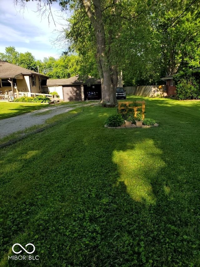 view of yard with fence, a garage, and driveway