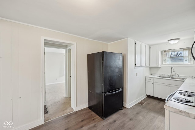 kitchen featuring wood finished floors, freestanding refrigerator, a sink, light countertops, and white cabinets